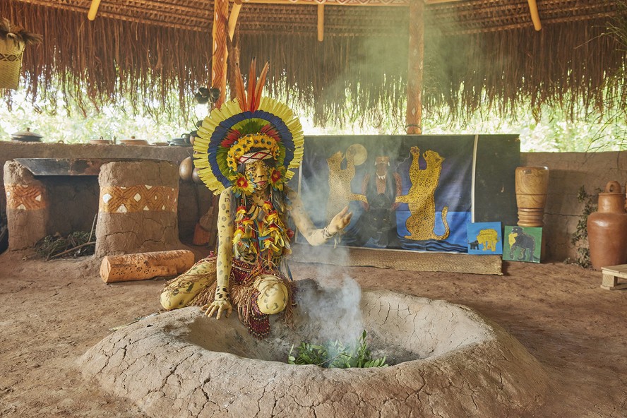 Tamikuã no centro da 'casa de fazer farinha', espaço em que transmite a cultura indígena para crianças da comunidade através de cânticos, alimentos tradicionais e aulas de guarani