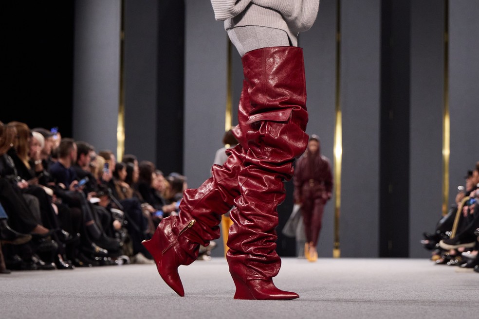Botas em burgundy aparecem super drapeadas e acima do joelho — Foto: Getty Images